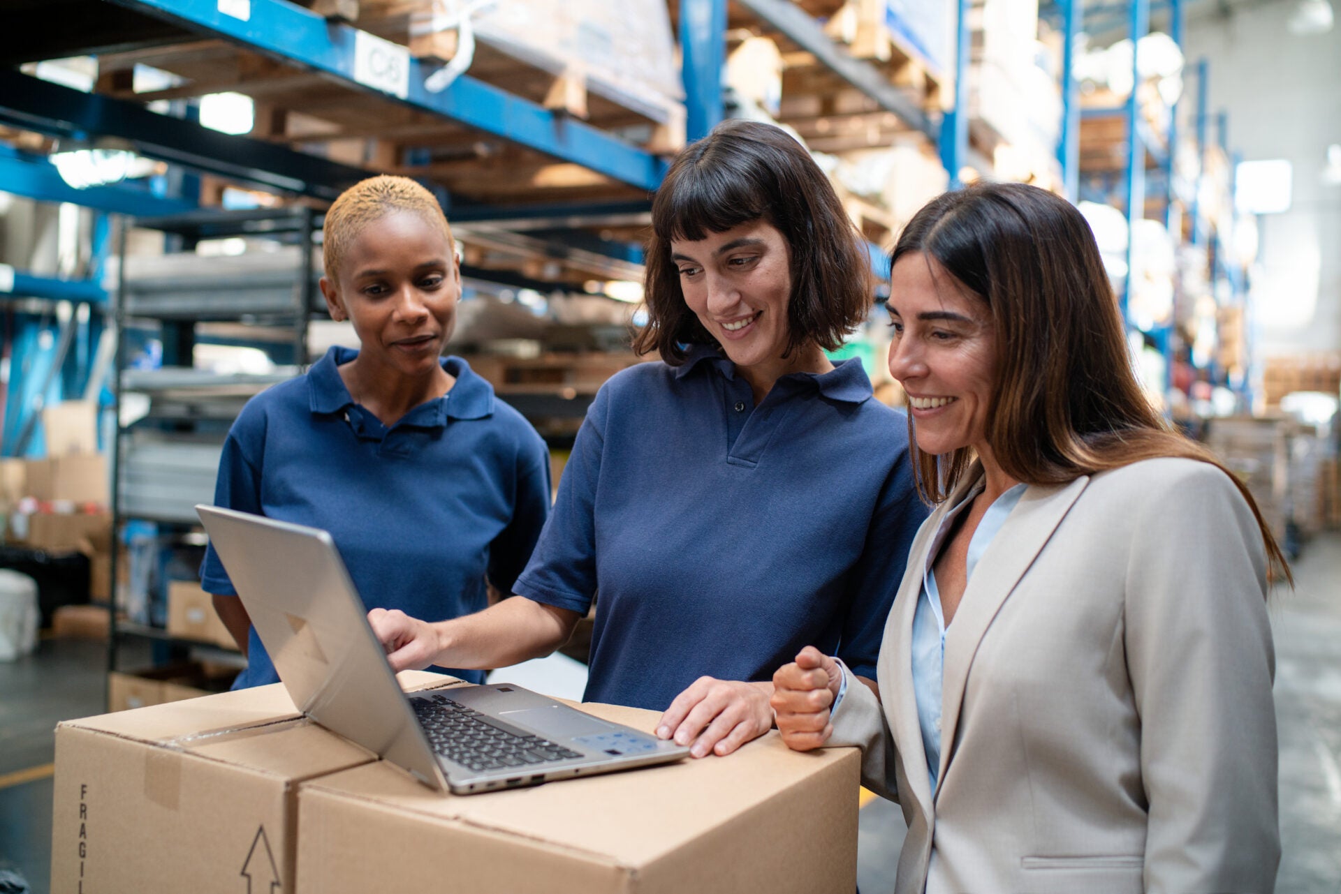 Worker using laptop discussing delivery schedules with warehouse manager